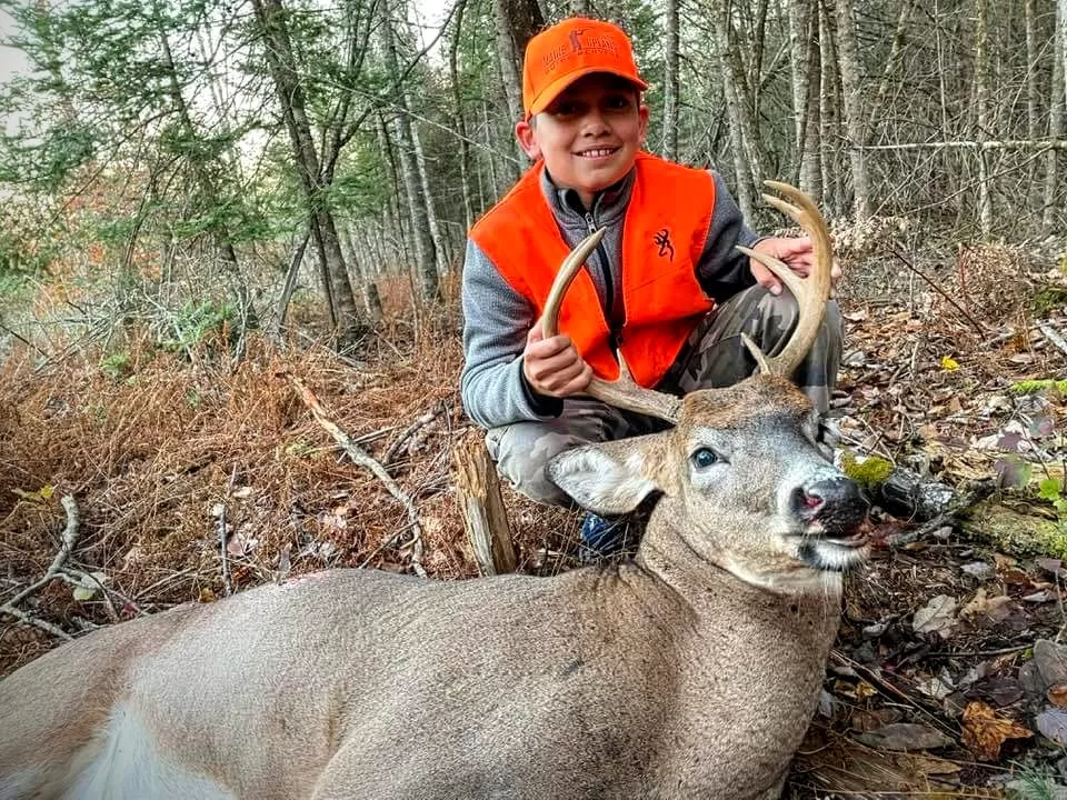 young boy poses with large buck after successful hunt