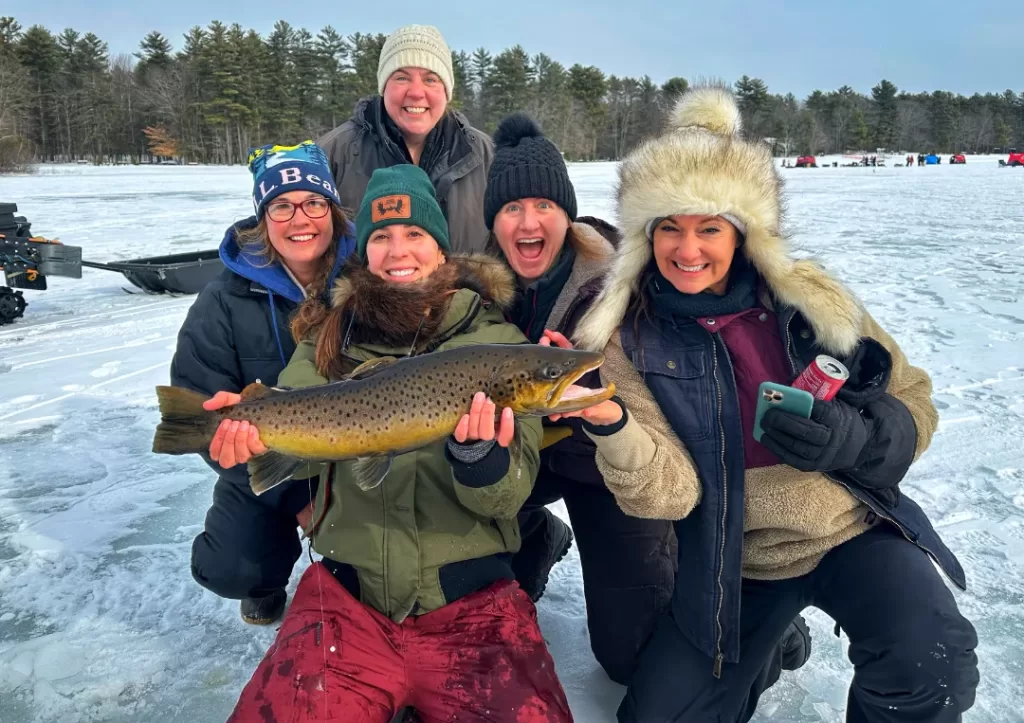 group of women hold a large trout on an ice fishing trip