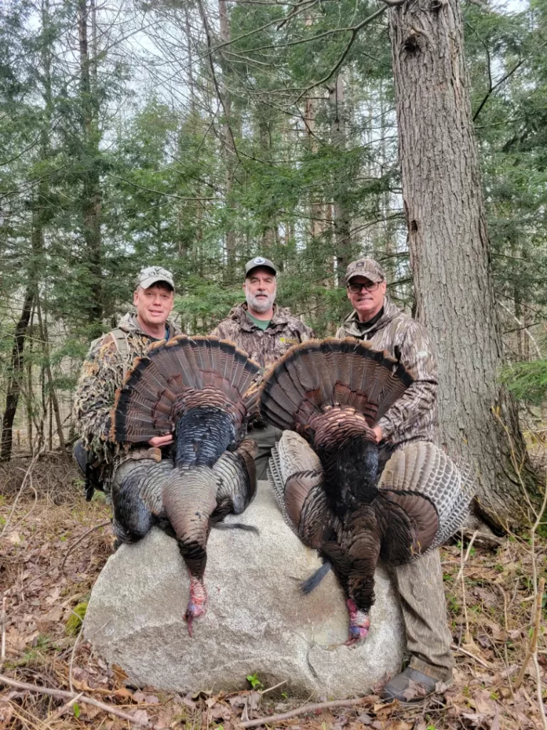three hunters hold up two turkeys after a successful hunt