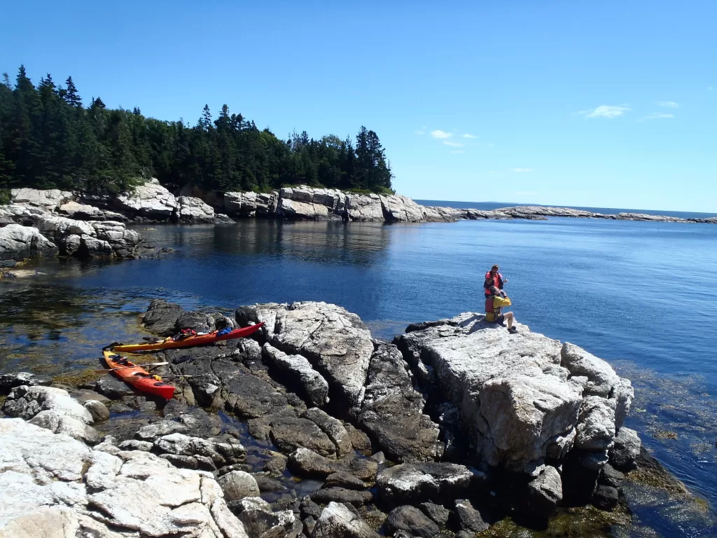 two sea kayakers sitting on a large rock with their kayaks behind them
