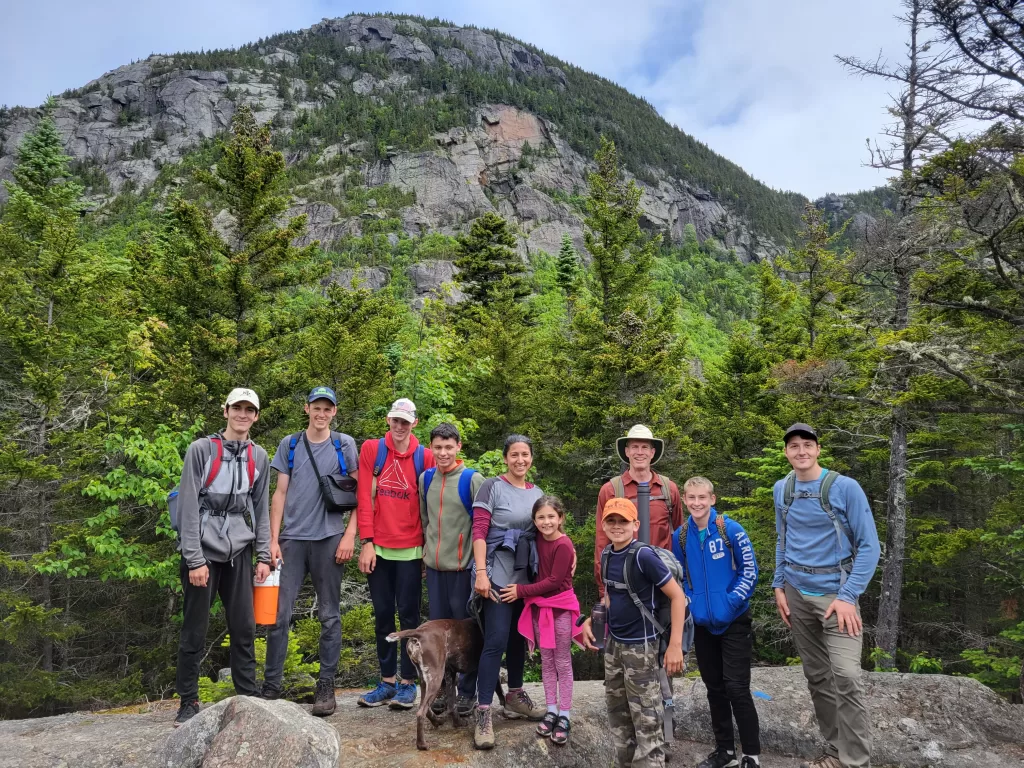 a group of maine hikers stand together with a rocky peak behind them