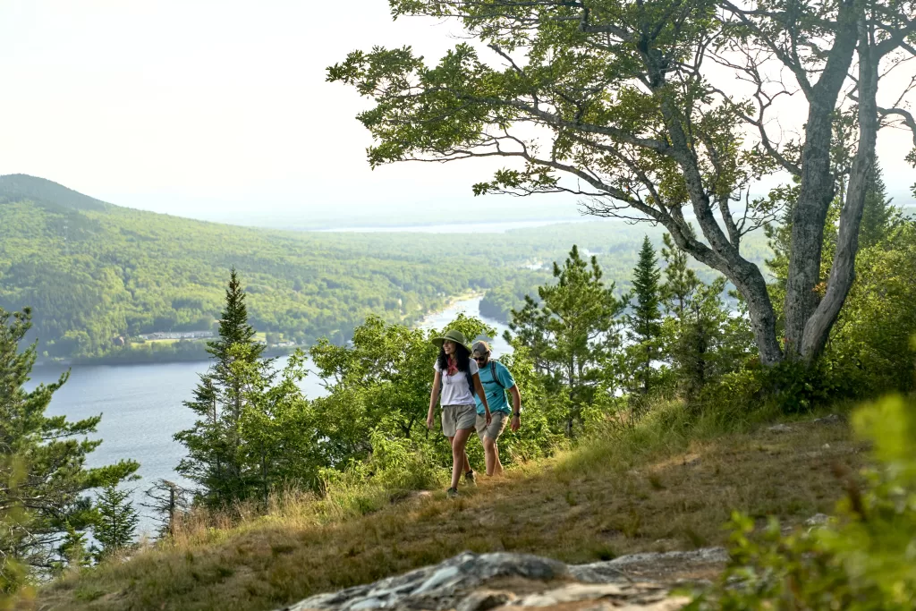 a man and woman hiking in the maine woods above a lake