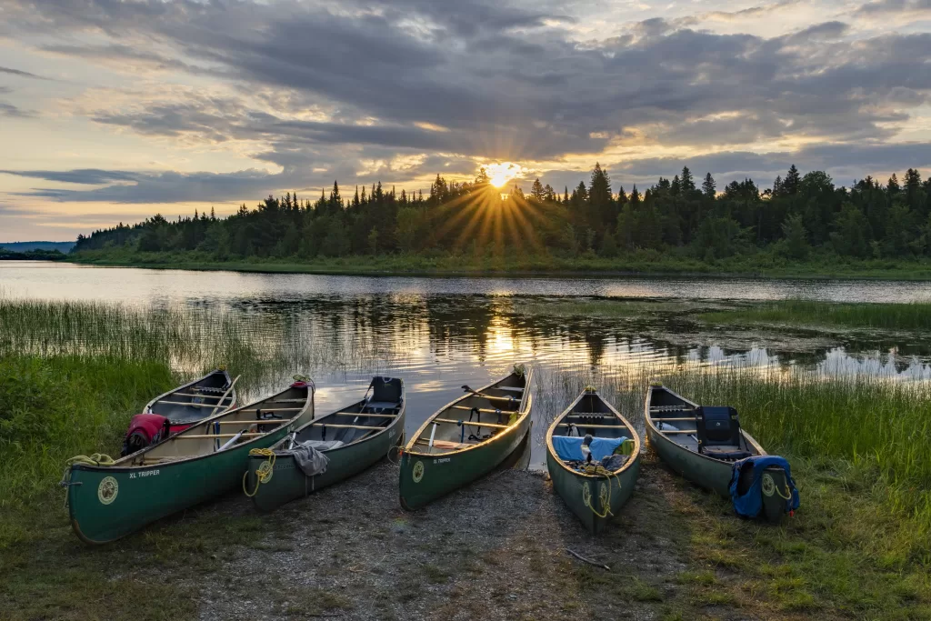 six canoes on a riverbank with the sun setting behind them