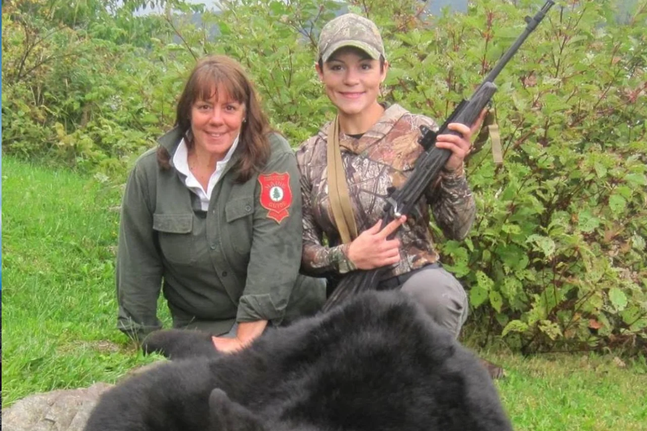 A Maine Guide and a young hunter crouching in front of a bear
